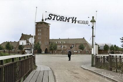 In ons archief vonden wij deze zwart-wit foto genomen door de NSB fotodienst. Op zogenaamde contactafdrukken. Deze foto hebben we ingekleurd. Deze foto maakte dat we meer wilde weten over de achtergrond. De foto is genomen bij de Veemarkt in Den Bosch. Het is vrij uniek omdat men nog over een bruggetje moest om het terrein te betreden. Op de foto is een spandoek te zien met de tekst; “Storm SS weekblad”. Het is een spandoek dat de propaganda uiting goed laat zien. Het tijdschrift “Storm SS” werd uitgegeven door de Nederlandse SS om publiek geïnteresseerd te krijgen en lid te laten worden in de gedachtengoed van de SS.